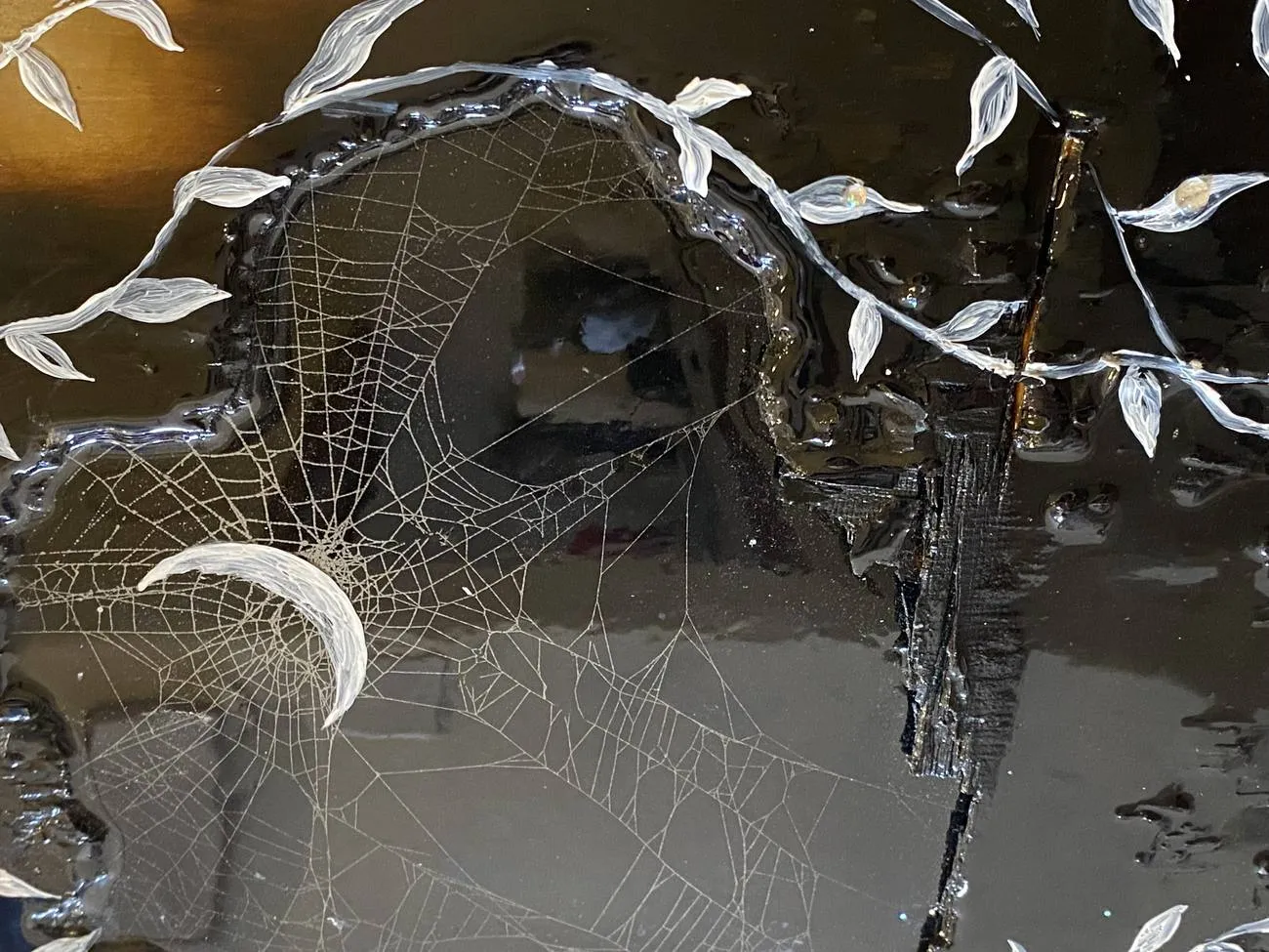 Detail — a preserved web and a crescent moon set in resin over wood.